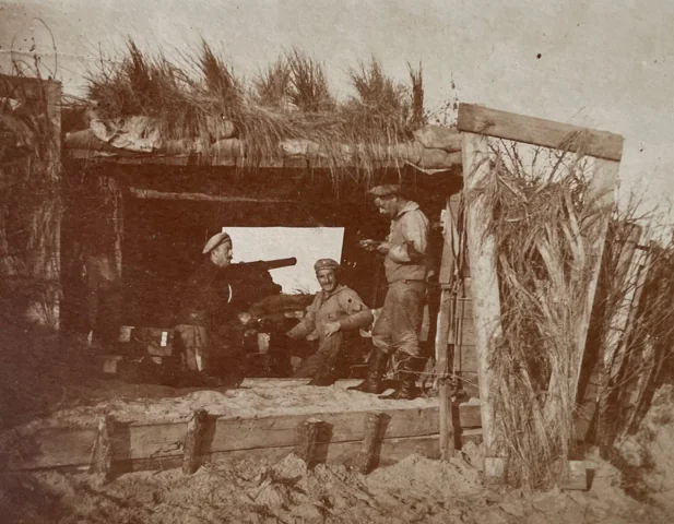 Three uniformed men beside a large gun emplacement.