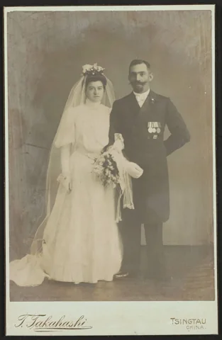 Wedding pair on a mounted studio print, with T. Takahashi and Tsingtau China printed below.