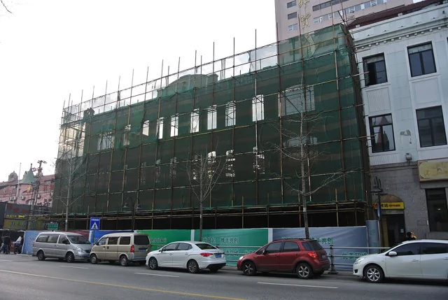 Former studio building covered in scaffolding and green construction netting.